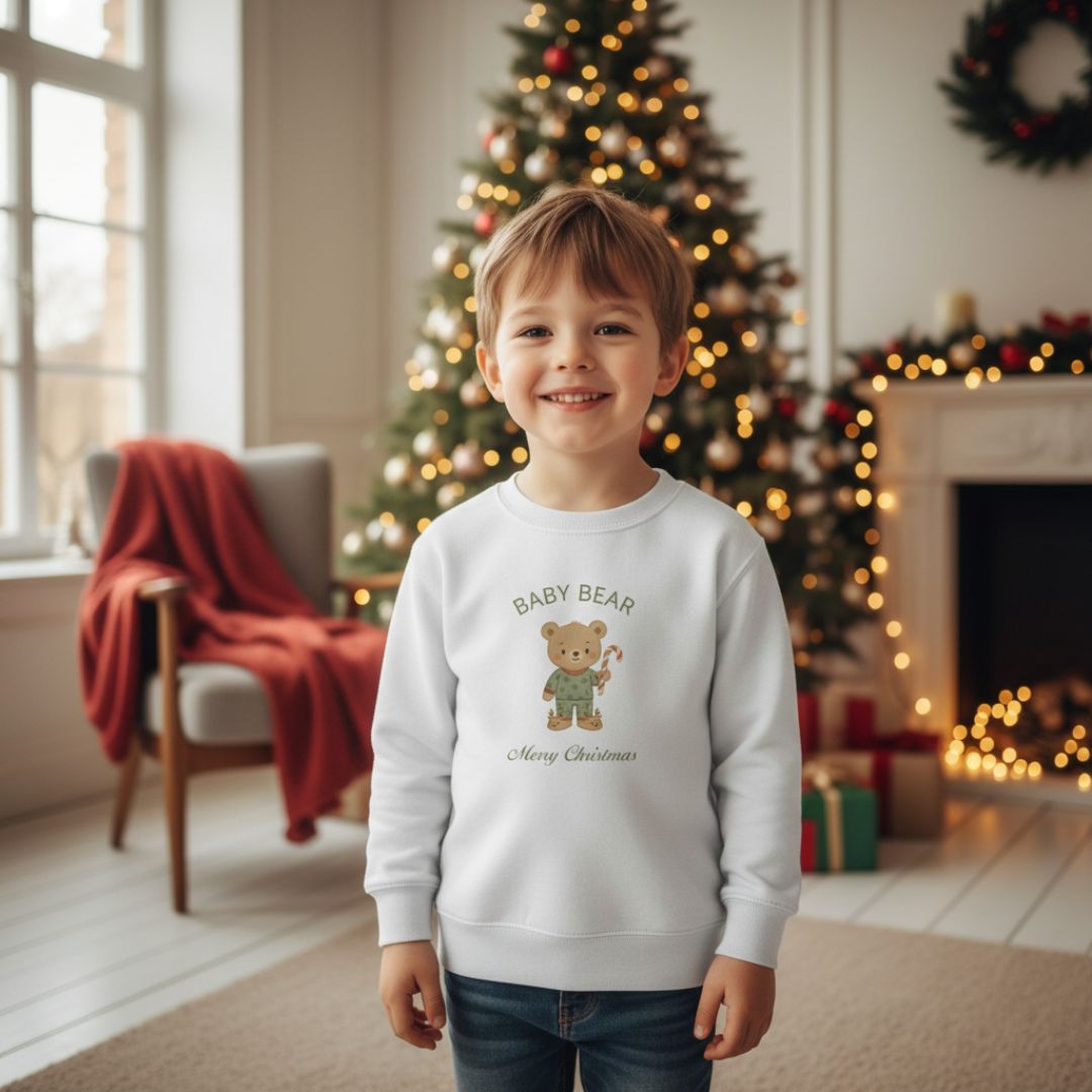 Junge trägt das weiße Weihnachts Sweatshirt - Bärenfamilie mit 'Baby Bear'-Motiv vor einem geschmückten Baum. Perfekt für festliche Kinderbekleidung.