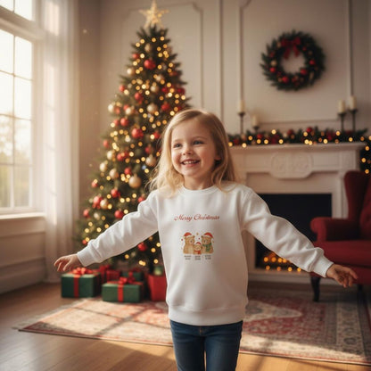 Mädchen in weißem Weihnachts Sweatshirt - Bärenfamilie mit fröhlichem Design vor einem Weihnachtsbaum. Ideal für nachhaltige und bequeme Kinderkleidung.